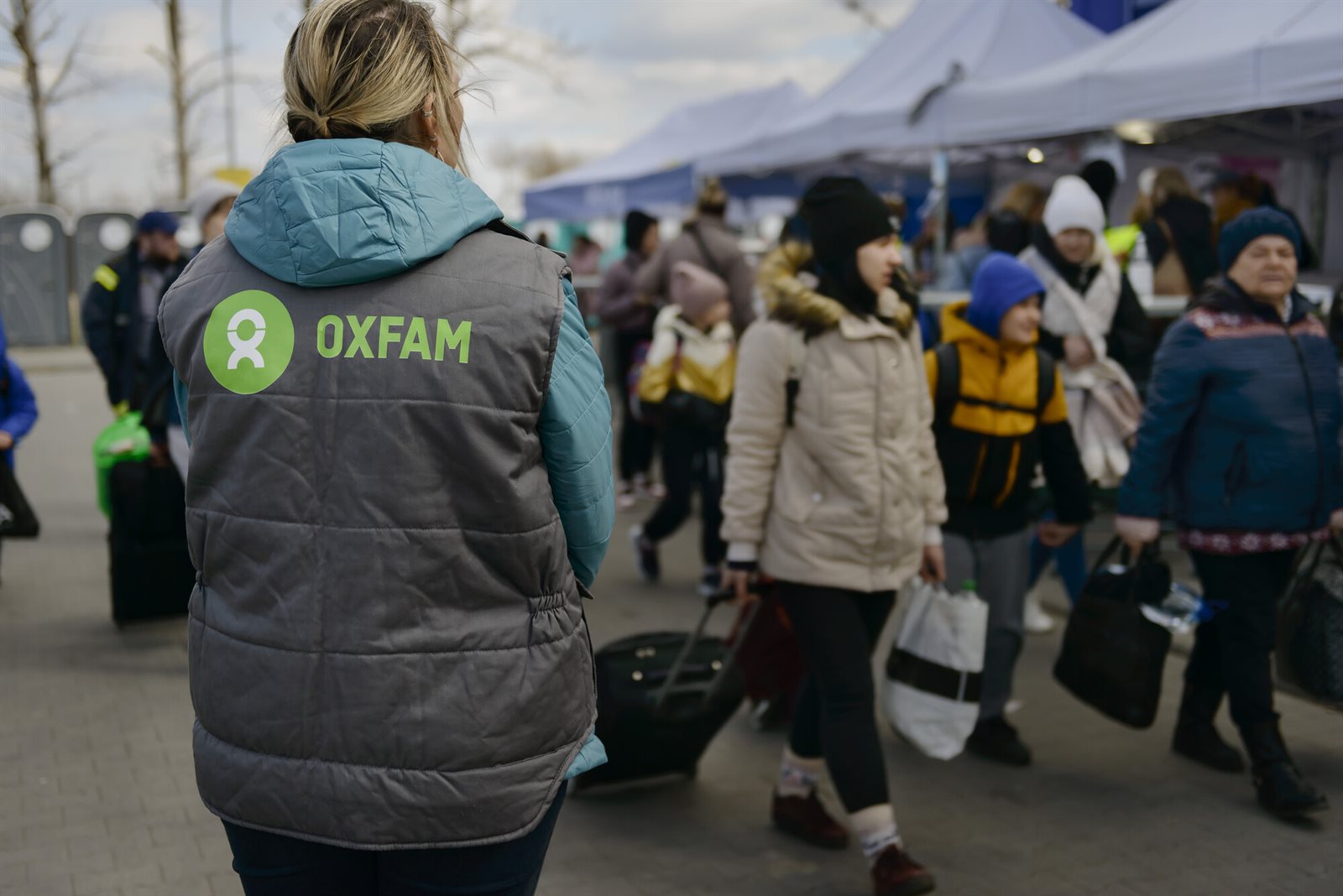 Vluchtelingen aan de grens, onderweg met hun spullen, samen met een Oxfam-medewerker vanaf de rug gezien.