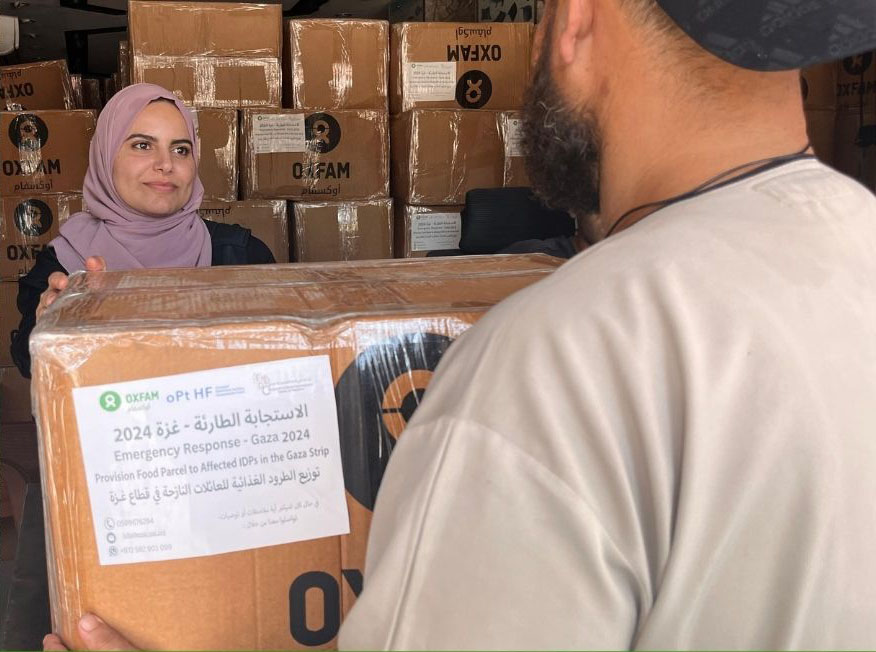 Een vrouw ontvangt een doos met hulpgoederen met daarop het Oxfam-logo