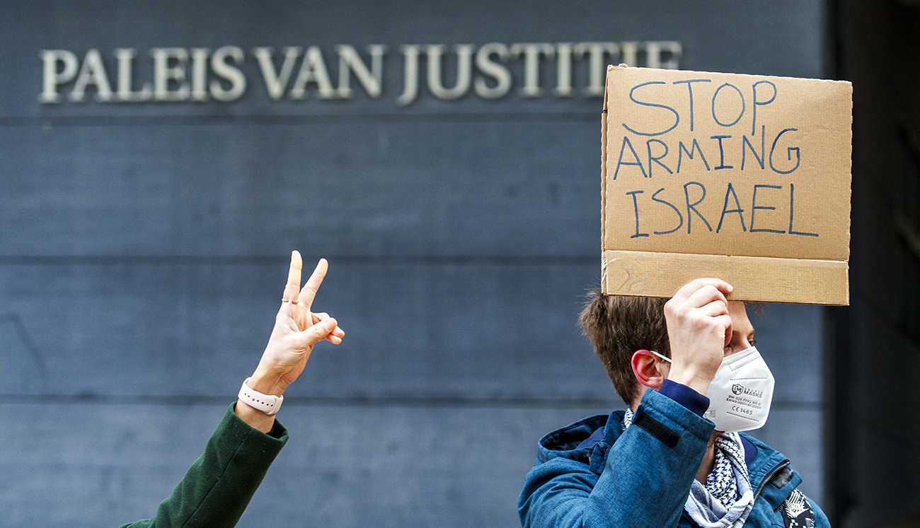 Een man staat voor het Paleis van Justitie met een bordje met daarop de tekst 'Stop arming Israel'
